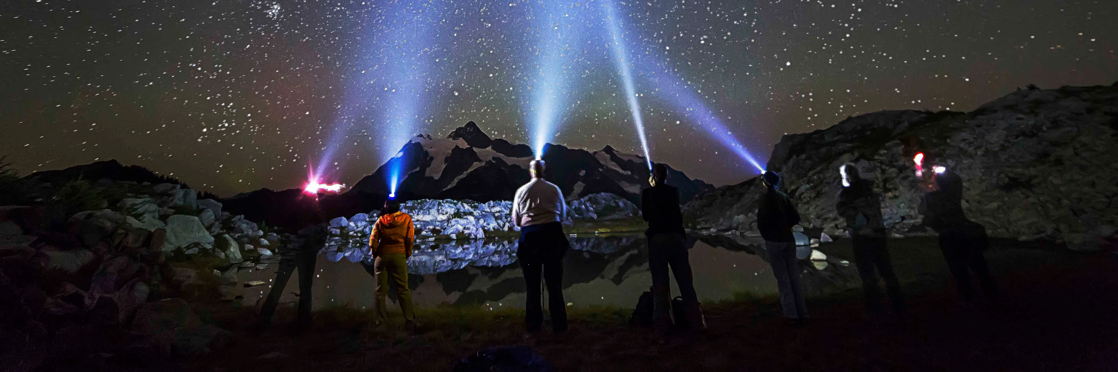 Stargazers with headlamps beside a tarn on Artist Ridge at night, Mount Shuksan silhouetted under the Milky Way