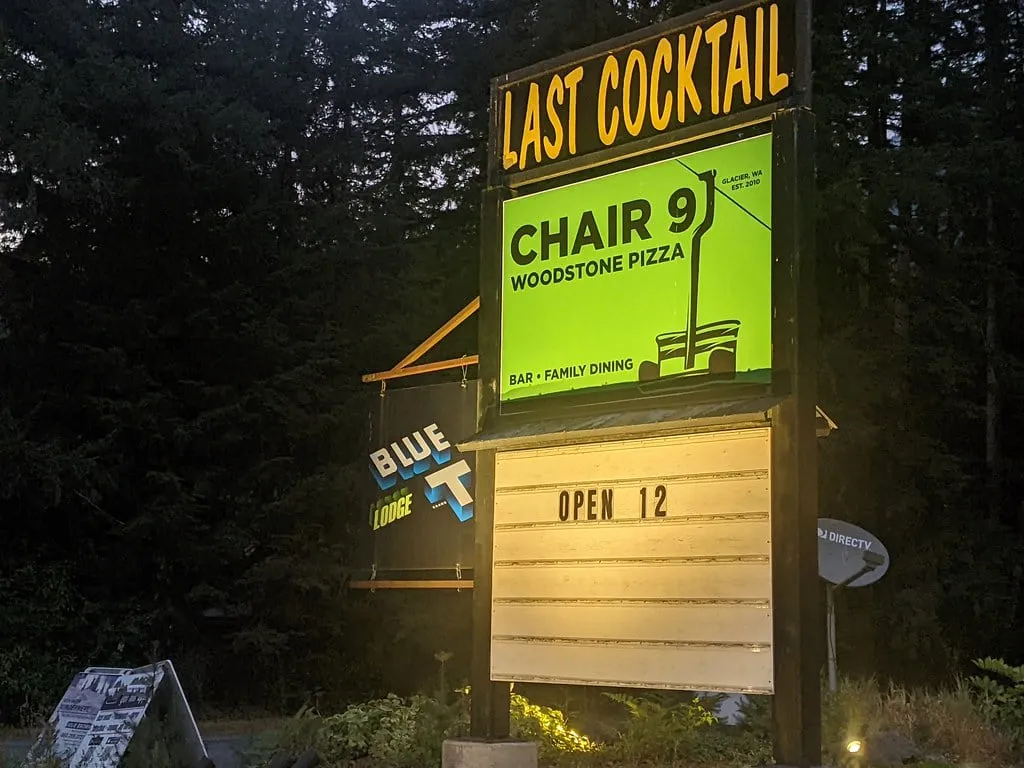 The illuminated roadside sign for Chair 9 Woodstone Pizza in Glacier, Washington reading Last Cocktail and Open 12