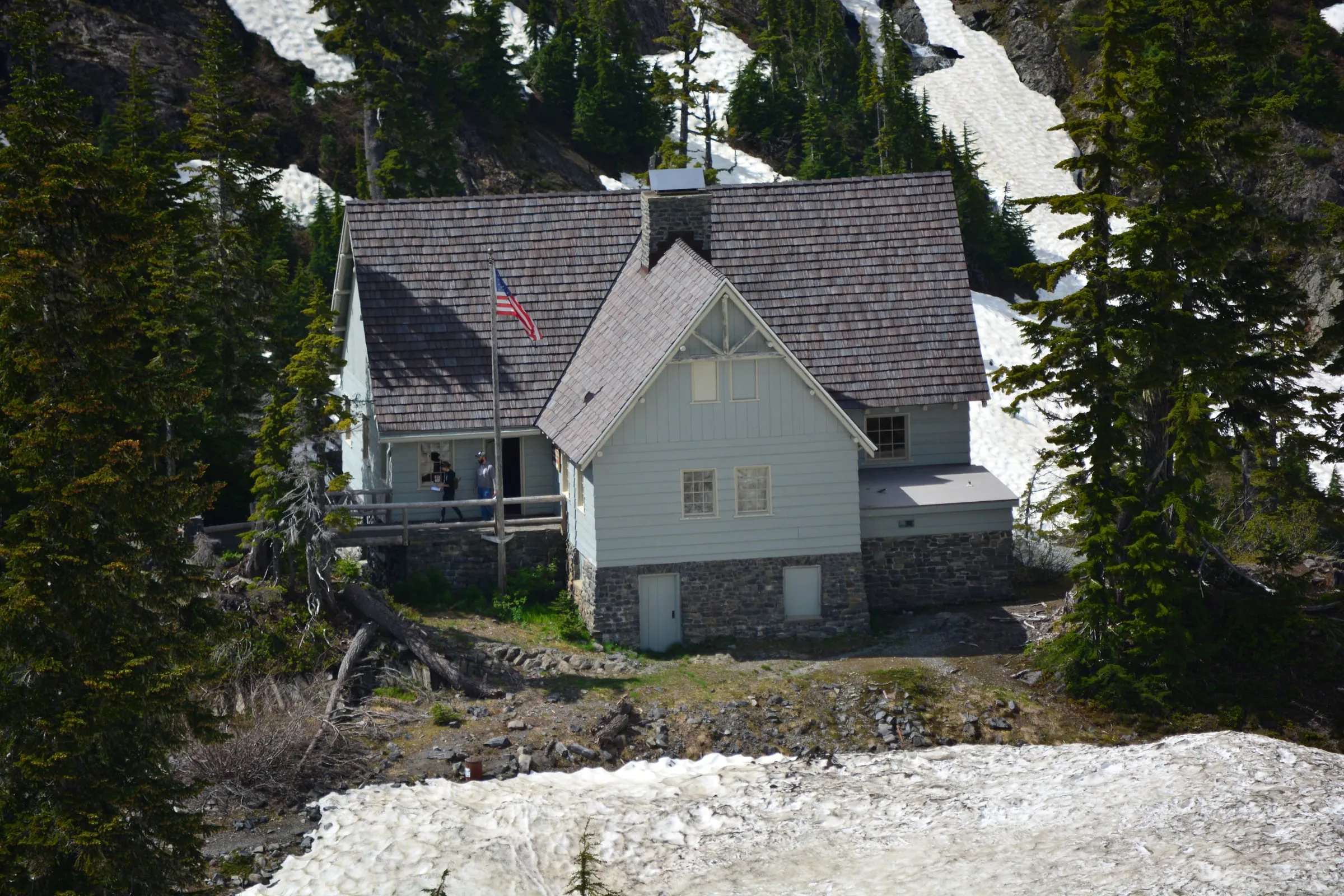 The stone-and-shingle Heather Meadows Visitor Center with snow still lying on the slopes around it in early summer