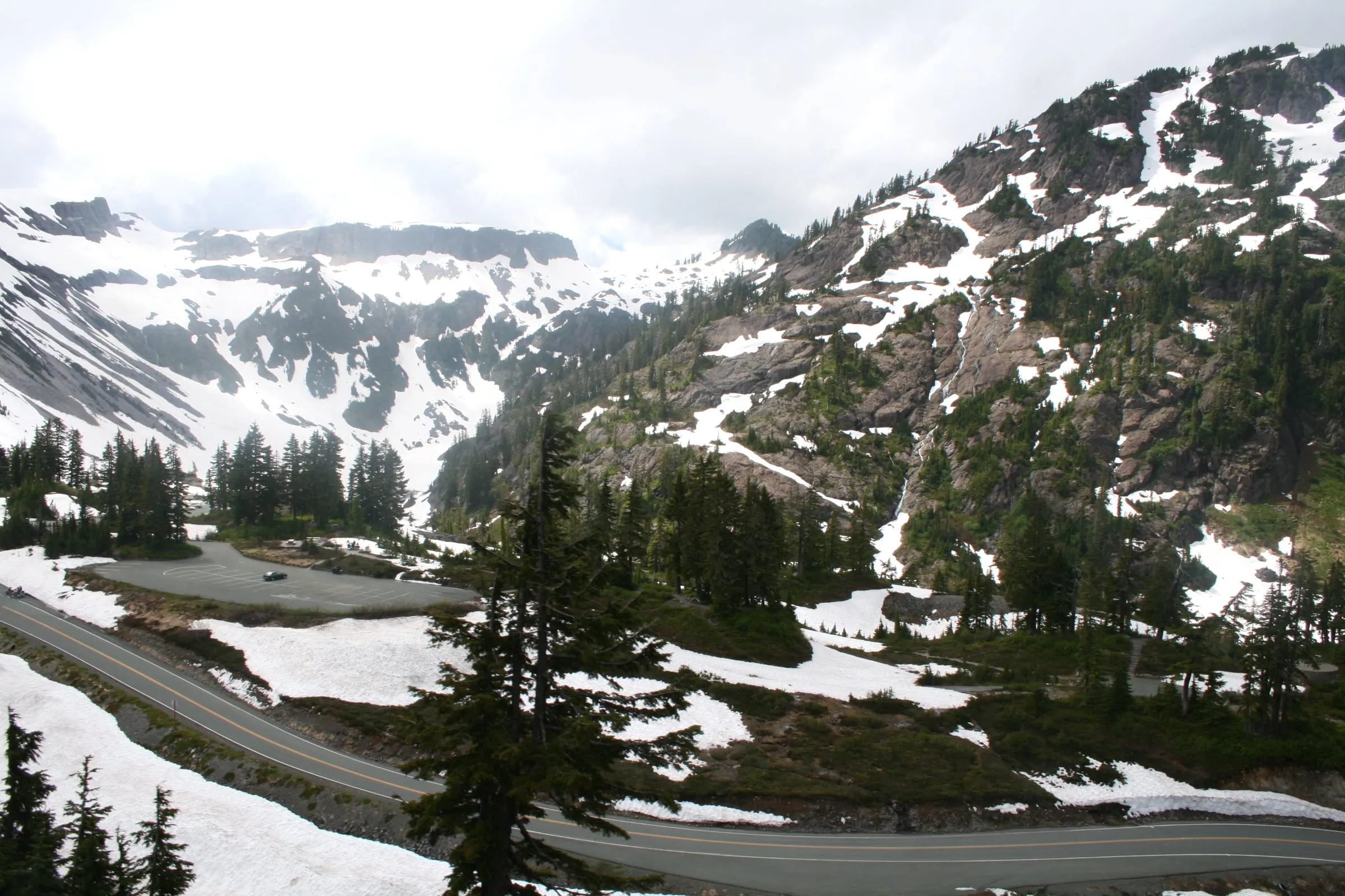Cars in the upper parking area at Mt. Baker Ski Area with the Mt. Baker Highway switchback and snow-streaked ridges above