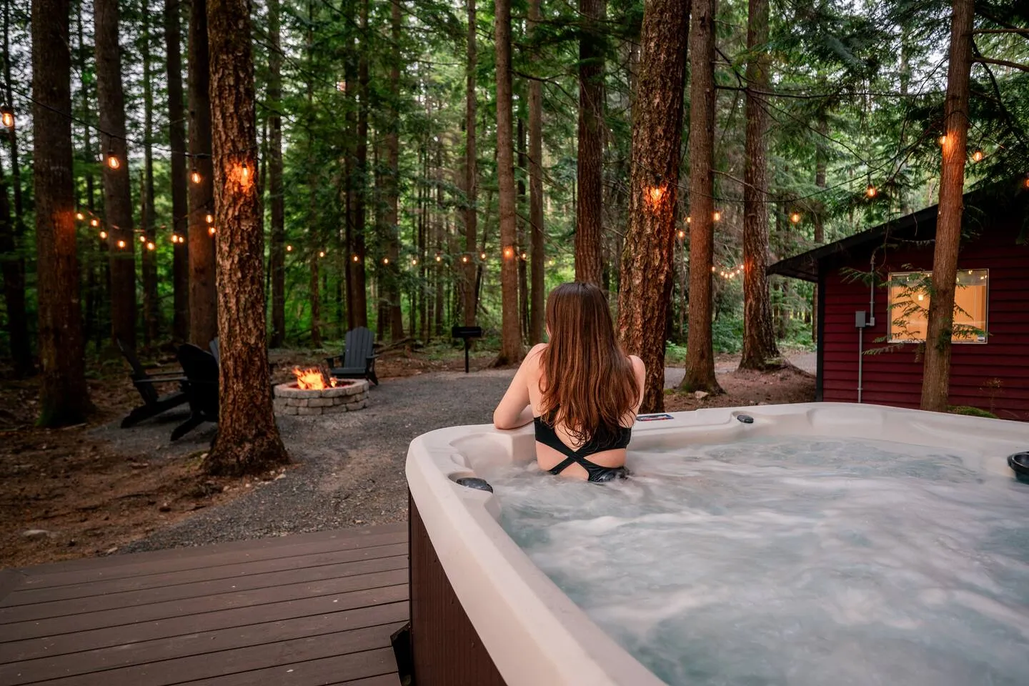 Guest relaxing in the private hot tub outside the red cabin, surrounded by evergreen forest